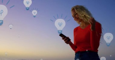 Günbatımında akıllı telefon kullanan beyaz bir kadının orta bölümündeki ampul simgelerinin canlandırılması. küresel bağlantılar, sosyal medya, teknoloji ve dijital arayüz konsepti dijital olarak oluşturulmuş video.