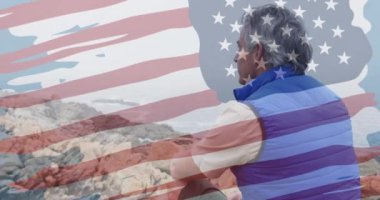 Dağlarda kayaların üzerinde oturan yaşlı beyaz adam üzerinde Amerikan bayrağı animasyonu. Vatanseverlik ve kutlama konsepti dijital olarak oluşturulmuş video.
