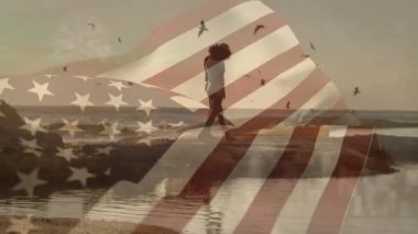 Sahildeki Afro-Amerikan çifti üzerine Amerikan bayrağının animasyonu. Vatanseverlik ve kutlama konsepti dijital olarak oluşturulmuş video.