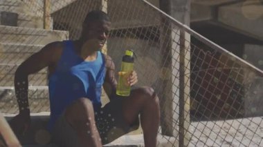 Yüzen sarı noktalar ve merdivenlerde oturan yorgun Afro-Amerikan fit adama karşı havai fişekler. Spor, spor ve teknoloji konsepti