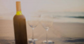 Obrázek zlatých teček na rozmazané láhvi červeného vína na pláži. vinařství, degustace a oslavy koncept digitálně generovaný image.