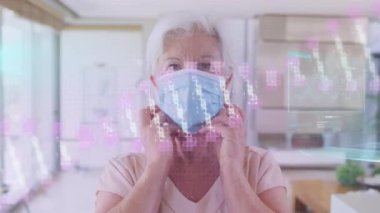 Yüz maskesi takan yaşlı beyaz bir kadının veri işleme animasyonu. covid 19 pandemik kavramı dijital olarak oluşturulan video sırasında küresel tıp ve dijital arayüz.