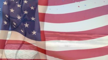 Amerikan bayrağı ve konfeti animasyonu plajdaki beyaz kadın üzerinde. Vatanseverlik ve kutlama konsepti dijital olarak oluşturulmuş video.