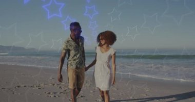 Neon yıldızlarının animasyonu, mutlu Afrika kökenli Amerikalı çiftin sahilde yürümesi üzerine renk değiştiriyor. Romantik aşk, ilişki ve birliktelik kavramı dijital olarak oluşturulmuş video.