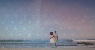 Sahilde yürüyen Afrikalı Amerikalı bir çiftin arkasındaki yıldızların animasyonu. Romantik aşk, ilişki ve birliktelik kavramı dijital olarak oluşturulmuş video.