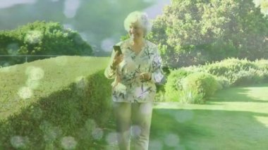 Beyaz tenli ihtiyarlara karşı akıllı telefon kullanan ve bahçede yürüyen ışıkların birleşik videosu. Ulusal Yürüyüş Günü Farkındalığı