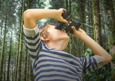 Composite image of caucasian boy with binoculars against tall trees in background. childhood and hobby concept