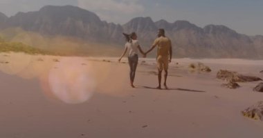 Multiple light spots floating against african american couple holding hands walking at the beach. travel and vacation concept