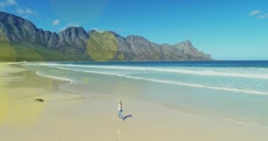 Multiple light spots floating against caucasian woman walking at the beach. travel and vacation concept
