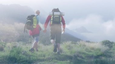 Composite video of clouds against caucasian couple hiking on the mountains. national walking day awareness concept