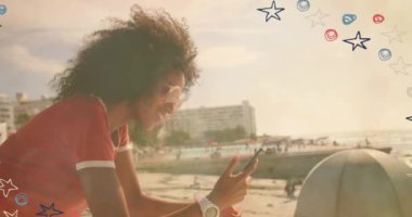 Colorful star icons against african american woman using smartphone near the beach. social media networking and technology concept