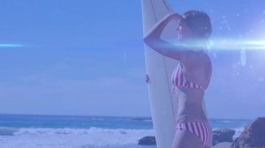 Işık animasyonu, elinde sörf tahtası olan mutlu beyaz kadın üzerinde ve uzaklığa bakıyor. su sporları, aktif yaşam tarzı ve tatiller dijital olarak üretilen video konsepti.