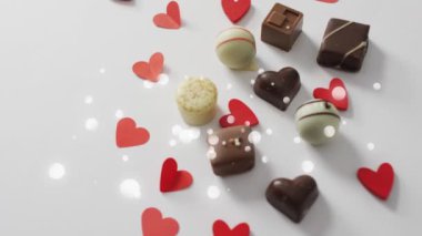 Çikolatalı pralinaların üzerindeki noktaların ve beyaz yüzeydeki kağıt kalplerin animasyonu. tatlılar, tatlılar ve dijital olarak üretilen çikolata konsepti.