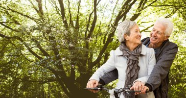 Smiling caucasian senior couple looking at each other while riding bicycle against trees in park. love, togetherness, nature, transportation, unaltered, senior citizens, retirement and awareness.