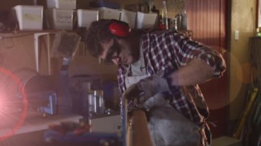 Animation of glowing light over caucasian man working in workshop. labor day, work, workers, tradition and celebration concept digitally generated video.
