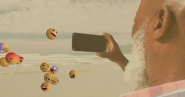 Animation of media icons over senior african american man taking selfie on sunny beach. healthy and active beach holiday concept digitally generated video.
