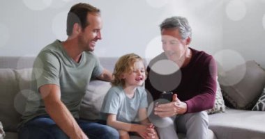 Animation of bokeh over happy grandfather, father and son on sofa. family, relationship and spending quality time together concept digitally generated video.