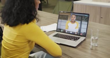 Çift ırklı iş kadını, Afrikalı Amerikalı iş arkadaşıyla görüntülü konuşma yapmak için dizüstü bilgisayar kullanıyor. ticari iletişim teknolojisi, dijital kompozit video.