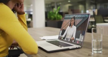 Çift ırklı iş arkadaşlarıyla video görüşmesi için bilgisayarını kullanan Afrikalı Amerikalı bir iş kadını. ticari iletişim teknolojisi, dijital kompozit video.
