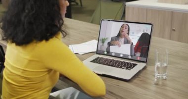 Afro-Amerikalı bir kadının beyaz kadın bir iş arkadaşıyla laptopta görüntülü konuşma yaptığı video. iş, işbirliği ve ofiste dijital olarak üretilen teknoloji konseptiyle çalışmak.