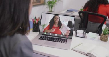 Kafkasyalı bir kadının çift ırklı bir iş arkadaşıyla laptopta görüntülü konuşma yaptığı video. iş, işbirliği ve ofiste dijital olarak üretilen teknoloji konseptiyle çalışmak.