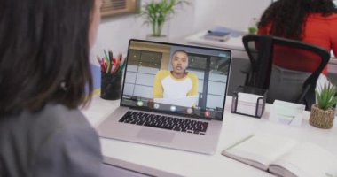 Kafkasyalı bir kadının çift ırklı bir iş arkadaşıyla laptopta görüntülü konuşma yaptığı video. iş, işbirliği ve ofiste dijital olarak üretilen teknoloji konseptiyle çalışmak.