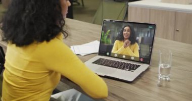 Afrikalı Amerikalı bir kadının çift ırklı bir iş arkadaşıyla bilgisayarında görüntülü konuşma yaptığı video. iş, işbirliği ve ofiste dijital olarak üretilen teknoloji konseptiyle çalışmak.