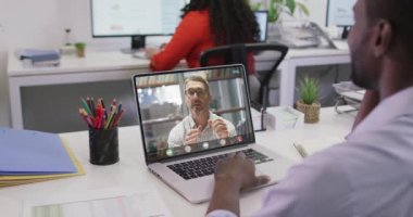 Afro-Amerikan bir adamın beyaz erkek iş arkadaşıyla laptopta görüntülü konuşma yaptığı video. iş, işbirliği, dijital kaynaklar ve dijital ortamda üretilen teknoloji konseptiyle çalışmak