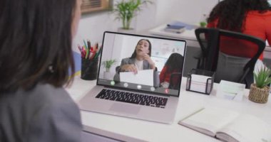 Kafkasyalı bir kadının çift ırklı bir iş arkadaşıyla laptopta görüntülü konuşma yaptığı video. iş, işbirliği ve ofiste dijital olarak üretilen teknoloji konseptiyle çalışmak.