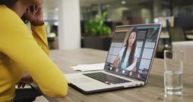 Afro-Amerikalı bir kadının beyaz kadın bir iş arkadaşıyla laptopta görüntülü konuşma yaptığı video. iş, işbirliği ve ofiste dijital olarak üretilen teknoloji konseptiyle çalışmak.