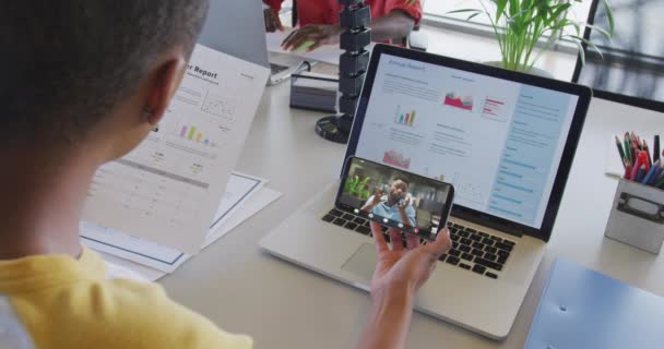 アフリカ系アメリカ人男性の同僚とスマートフォンでビデオ通話をしている出生女性のビデオ ビジネス オフィスでの作業技術コンセプトデジタルで生成されたビデオ — ストック動画