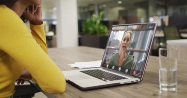 Kafkasyalı iş arkadaşıyla görüntülü konuşma yapmak için bilgisayarını kullanan iki ırklı bir iş kadını. ticari iletişim teknolojisi ve dijital kompozit video.