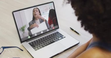 Çift ırklı iş arkadaşlarıyla video görüşmesi için bilgisayarını kullanan Afrikalı Amerikalı bir iş kadını. ticari iletişim teknolojisi ve dijital kompozit video.