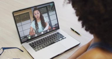 Çift ırklı iş arkadaşlarıyla video görüşmesi için bilgisayarını kullanan Afrikalı Amerikalı bir iş kadını. ticari iletişim teknolojisi ve dijital kompozit video.
