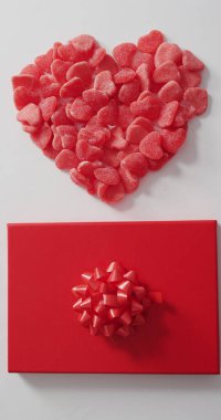 Kalp şeklindeki kırmızı şekerlerin dikey görüntüsü ve beyaza sarılmış hediye. Sevgililer Günü, romantizm ve kutlama.