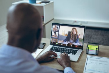 Afrikalı Amerikalı iş adamı iş arkadaşlarıyla çevrimiçi görüşmeler yapıyor. değiştirilmemiş, ofis, kablosuz teknoloji, video konferansı, internet, iş dünyası, takım çalışması.