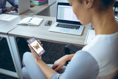 Genç Afro-Amerikan iş kadını ofiste çalışırken akıllı telefonları kontrol ediyor. değiştirilmemiş, iş dünyası, kablosuz teknoloji, ödenebilir olmayan jetonlar, finans, araştırma.