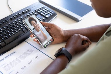 Afrika kökenli Amerikalı iş arkadaşları akıllı telefondan video görüşmeleri sırasında pazarlama raporlarını tartışıyor. değiştirilmemiş, ofis, çevrimiçi, teknoloji, video konferansı, tartışma, internet, iş, takım çalışması.
