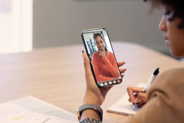 Afrika kökenli Amerikalı kadın iş arkadaşları ofisteki akıllı telefondan görüntülü arama yoluyla birlikte çalışıyorlar. değiştirilmemiş, çevrimiçi, teknoloji, video konferansı, tartışma, internet, iş, takım çalışması.