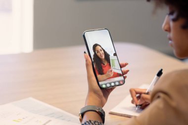 Çift ırklı iş kadını video görüşmesi sırasında kadın melez meslektaşıyla birlikte veri göstererek notlar alıyor. değiştirilmemiş, iş, kablosuz teknoloji, çalışma, toplantı, takım çalışması ve ofis konsepti.