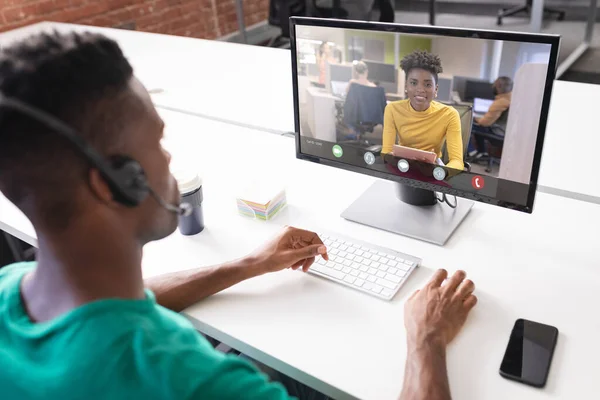 African american businesswoman during video call with african american male colleague in office. unaltered, business, technology, working, meeting and office concept.