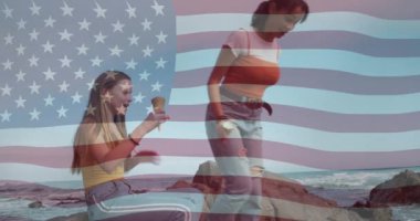 Animation of american flag over diverse female couple at beach. international youth day and celebration concept digitally generated video.