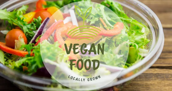 Image of vegan food locally grown text in green, over bowl of fresh salad on wooden boards. vegan day, organic vegetable produce and healthy eating concept digitally generated image.