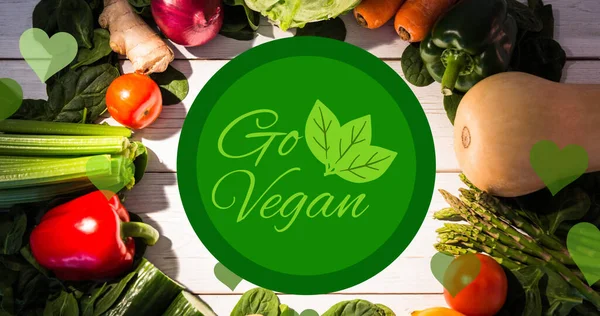 stock image Image of go vegan text in green with leaves logo, over fresh vegetables on white boards. vegan day, organic vegetable produce and healthy eating concept digitally generated image.