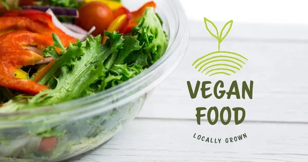 Image of vegan food text in green over fresh organic vegetable salad in bowl on wooden boards. vegan day, organic vegan produce and healthy eating concept digitally generated image.