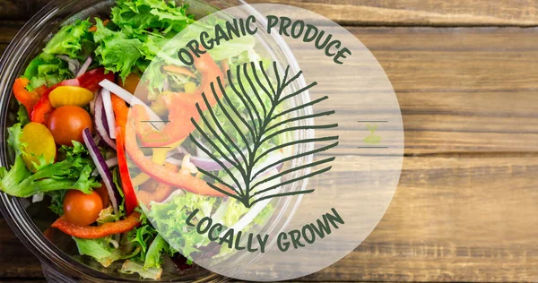 Image of locally grown organic produce text in green, over bowl of fresh salad on wooden boards. vegan day, organic vegetable produce and healthy eating concept digitally generated image.