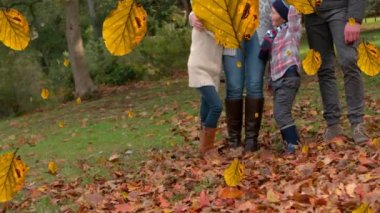 Sonbahar parkında güz yapraklarının mutlu beyaz bir ailenin üzerine düşmesi. Güz, zaman geçiyor, aile ve birliktelik kavramı dijital olarak oluşturulmuş video.