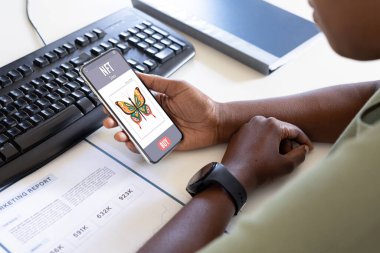 Afrika kökenli Amerikalı iş adamı ofisteki akıllı telefonları kontrol ederken rapor çalışıyor. değiştirilmemiş, iş yeri, ofis, kablosuz teknoloji, ödenemeyen jetonlar, finans, internet.