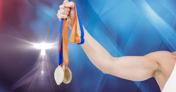 Hand holding multiple medals against spot of light on blue background with copy space. sports and competition concept