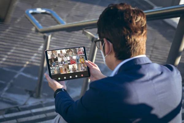 Asian businessman attending online meeting through digital tablet outside office. unaltered, wireless technology, video conference, discussion, internet, business, teamwork, covid.
